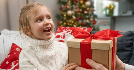 A young girl with an excited face as she receives a Christmas present