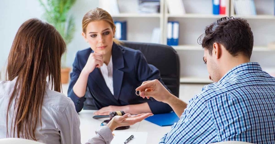 A man and woman sitting across from an attorney. The man is handing the woman next to him his wedding ring