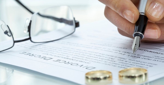 A person signing divorce papers as wedding rings rest on the paper