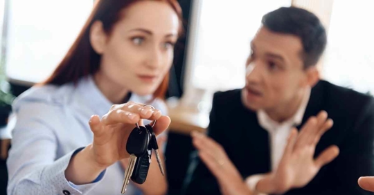 A woman passing keys over to someone while the man next to her objects. It's clear that they are arguing.